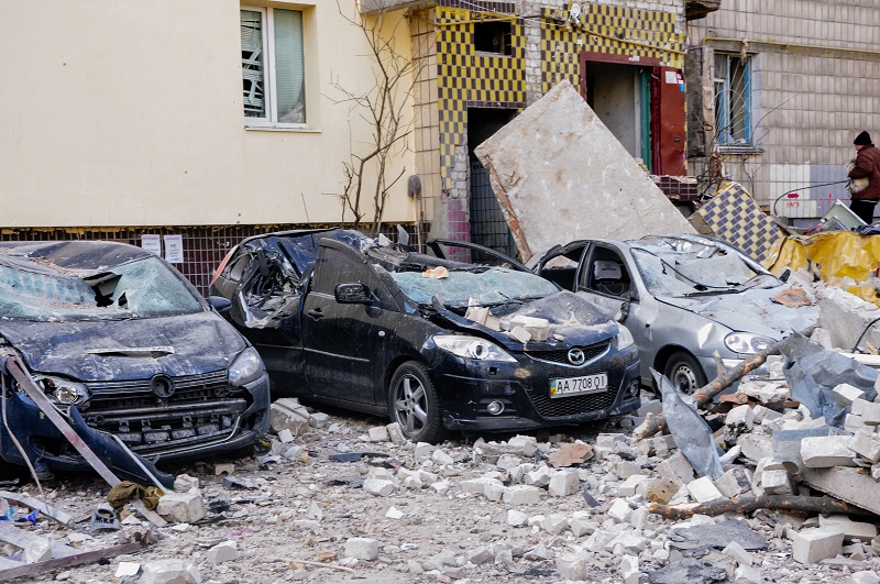 Zniszczone samochody stojące pod ostrzelanym blokiem mnieszkalnym w Kijowie